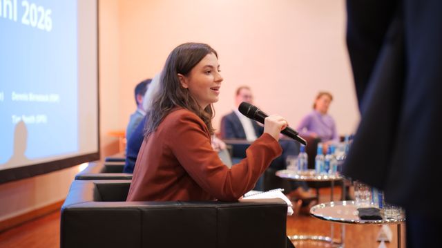 Clara Schweizer sitzt auf einem Sessel und hält ein Mikro in der Hand und spricht.